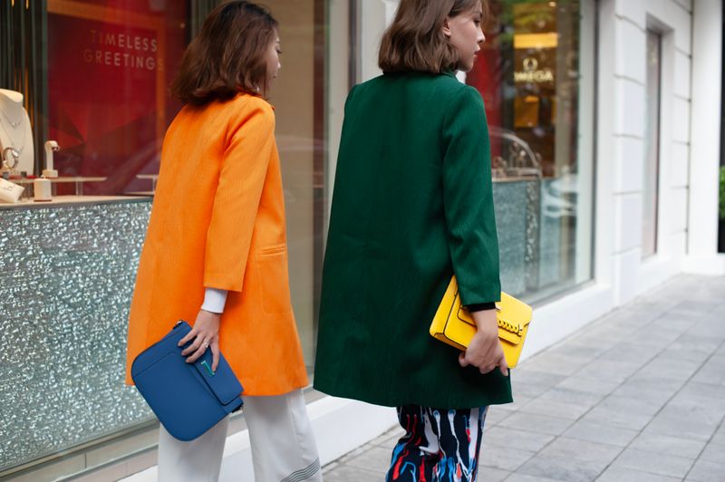 Two street-style outfits: an orange coat with a blue bag, and a green coat with a yellow bag